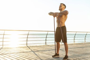Çıplak gövdeli genç atletik adam sabahın erken saatlerinde plajda spor yapıyor. Kas antrenmanı. Sağlıklı yaşam tarzı