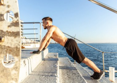 Spor kıyafetli atletik bir adam sabahın erken saatlerinde plajda şınav çekiyor.