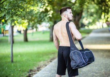 Çıplak gövdesi ve spor çantası olan genç bir sporcunun portresi.