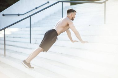 Atletik adam dışarıda merdivenlerde şınav çekiyor.