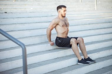 Atletik adam dışarıda merdivenlerde şınav çekiyor.