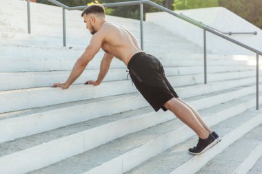 Atletik adam dışarıda merdivenlerde şınav çekiyor.