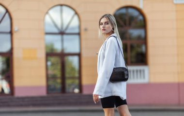 Beyaz ceketli, deri çantalı, modacı bir kadın. Sokak modası