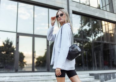 Şehirde poz veren modaya uygun giyinmiş sarışın bir kadın. Sokak modası