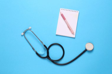 Mavi arka planda steteskoplu defter. Üst görünüm