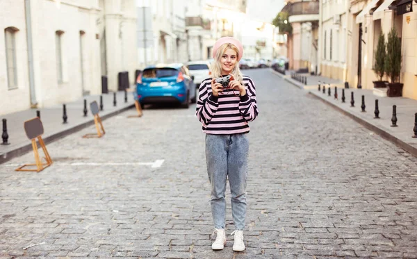 Şehirde retro kamerası olan bereli çekici bir hippi kız. Seyahat konsepti, yaşam tarzı. Fransız tarzı