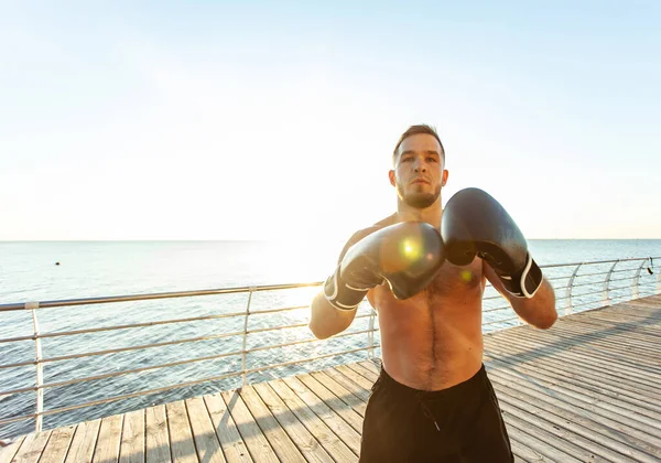 Athletic man in boxing gloves boxing in the early morning on the beach