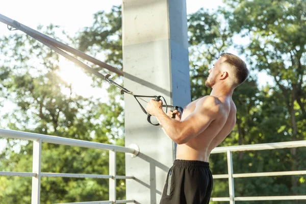 Genç kaslı erkek sporcu dışarıda dirençle egzersiz yapıyor. Fonksiyonel eğitim.