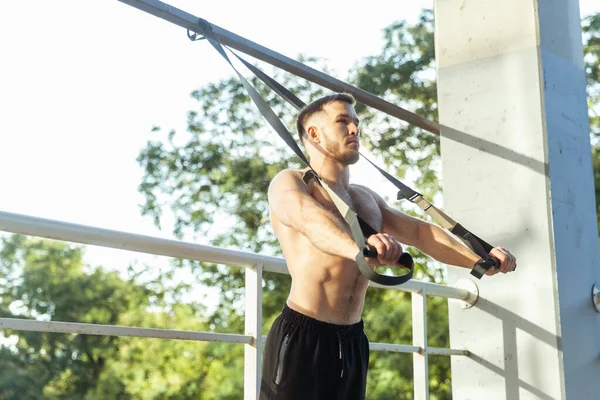 Genç kaslı erkek sporcu dışarıda dirençle egzersiz yapıyor. Fonksiyonel eğitim.
