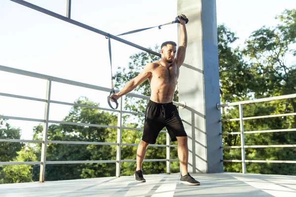 Genç kaslı erkek sporcu dışarıda dirençle egzersiz yapıyor. Fonksiyonel eğitim.