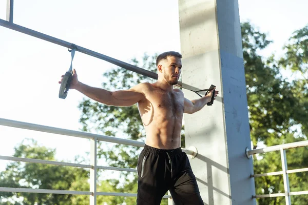 Genç kaslı erkek sporcu dışarıda dirençle egzersiz yapıyor. Fonksiyonel eğitim.
