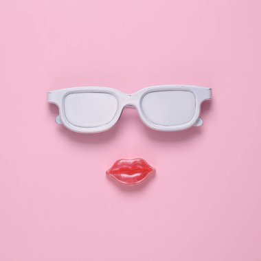 Pembe arka planda yüz şeklinde beyaz gözlük ve dudaklar. Konsept pop, çağdaş natürmort, minimal yerleşim