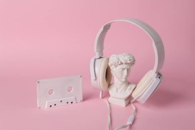 David 'in kulaklığı ve pembe arka planda ses kaseti olan antika büstü. Kavramsal patlama. Minimal natürmort. Yaratıcı müzik düzeni