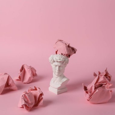 Pembe arka planda buruşuk kağıt topları olan antik David büstü. Kavramsal patlama. Minimal natürmort. Yaratıcı fikir