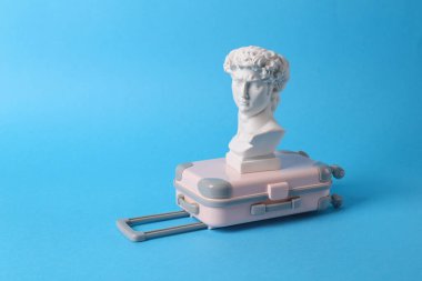 Antika David, mavi arka planda bavullarıyla baskın yaptı. Minimal natürmort. Yaratıcı seyahat turizmi kavramı