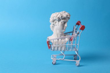 David 'in mavi arka planda alışveriş arabalı antika büstü. Kavramsal patlama. Minimum alışveriş hala hayattadır. Yaratıcı fikir