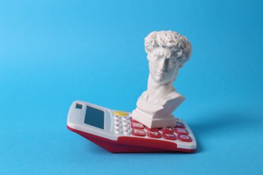 Antika David mavi arka planda hesap makinesiyle baskın yaptı. Kavramsal patlama. Minimal natürmort. Yaratıcı fikir