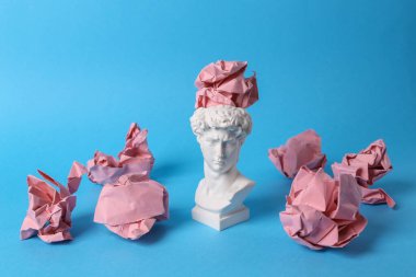Antika David 'in mavi arka planda buruşmuş kağıt toplarıyla büstü. Kavramsal patlama. Minimal natürmort. Yaratıcı fikir