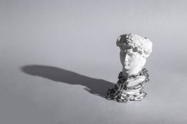 David 'in antika büstü gri arka planda çelik zincir sarılı. Kavramsal patlama. Minimal natürmort. Yaratıcı fikir