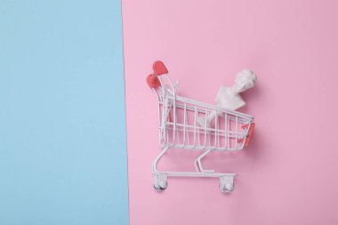 Venüs büstü pembe mavi arka planda alışveriş arabası. Yaratıcı düzen. Minimum alışveriş hala hayattadır. Düz yatıyordu. Üst görünüm