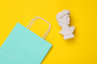 Sarı arka planda alışveriş torbası olan David Bust. Minimal natürmort. Düz yatıyordu