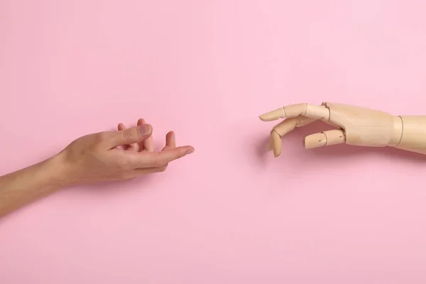 Wooden hand and human hand reach out to each other on pink background