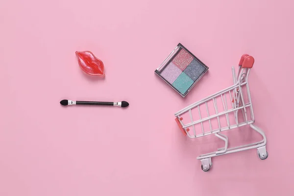 Beauty store. Shopping cart with cosmetics on pink background