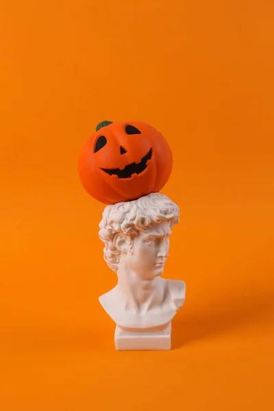 オレンジの背景にジャックランタンカボチャの頭を持つデビッドの石膏バスト ハロウィンのコンセプト ミニマルな静物写真 — ストック写真
