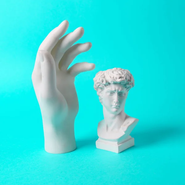 Antique David bust with statue hand on turquoise background. Minimal still life