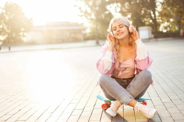 Young Smiling Woman Enjoying Music Headphones While Sitting Skateboard City — Stockfoto