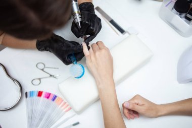 Manikür ustası, manikürcüde kadın elinin tırnaklarını elektrikli dosya makinesiyle söker.