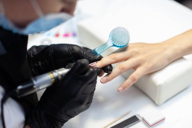 Manikür ustası, manikürcüde kadın elinin tırnaklarını elektrikli dosya makinesiyle söker.