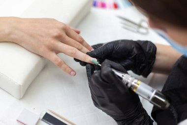 Manikür ustası, manikürcüde kadın elinin tırnaklarını elektrikli dosya makinesiyle söker.