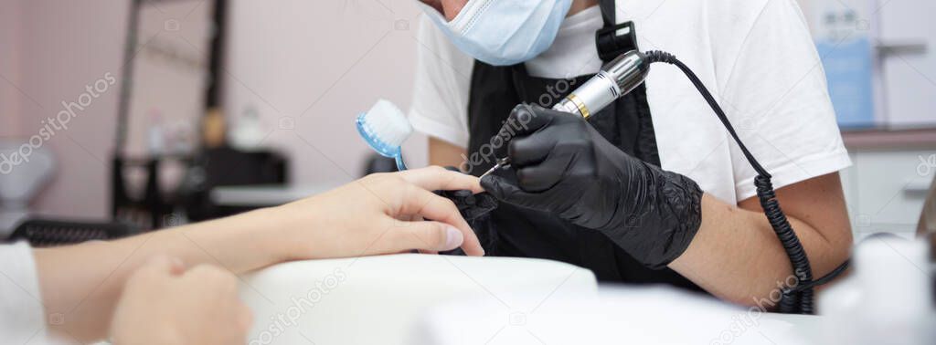 Manicure master removes cuticles with electric file machine on female hand in nail salon