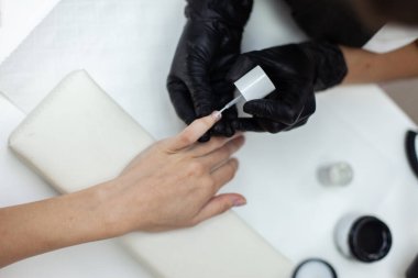 Manicurist paints with nail polish the nails of a woman's clint in nail salon. The working process