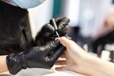 Manicurist paints with nail polish the nails of a woman's clint in nail salon. The working process