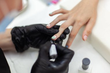 Manicurist paints with nail polish the nails of a woman's clint in nail salon. The working process