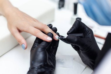 Manicurist paints with nail polish the nails of a woman's clint in nail salon. The working process