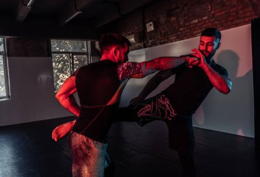 MMA dövüşçüleri spor salonunda neon ışıkta tekme ve savunma talimi yapıyorlar.