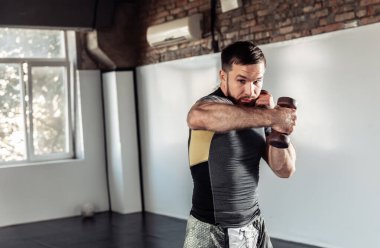 Atletik erkek boksör spor salonunda dambıllarla yumruk sallıyor.