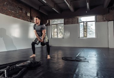 Spor salonunda kettlebell ile egzersiz yapan genç bir atletik.
