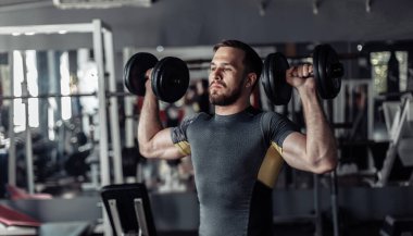 Athletic man exercising shoulder muscles with dumbbells in his hands