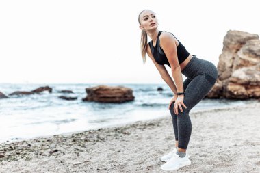 Beautiful tired fit woman resting after running or heavy workout on wild beach
