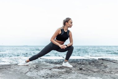 Beautiful young fit woman in sportswear training alone on urban beach. Healthy lifestyle concept