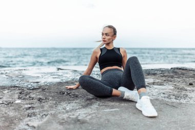Fit woman in sportswear sitting on urban beach