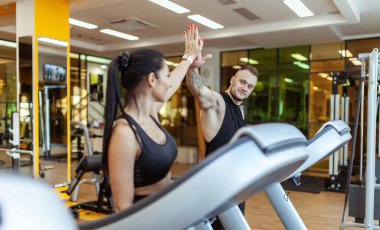 Athletic man and woman running on treadmill together and high five in gym