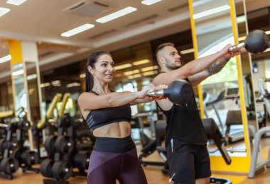 Athletic man and woman training together with kettlebells in modern gym