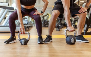 Athletic man and woman training together with kettlebells in modern gym