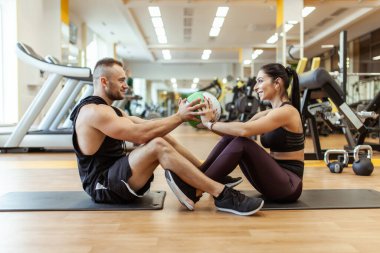Athletic man and woman are training together with medicine ball in modern gym. Healthy lifestyle