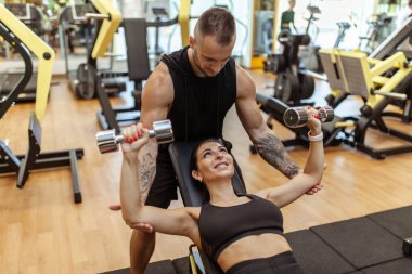 Young fit woman training muscles with personal trainer man in the gym